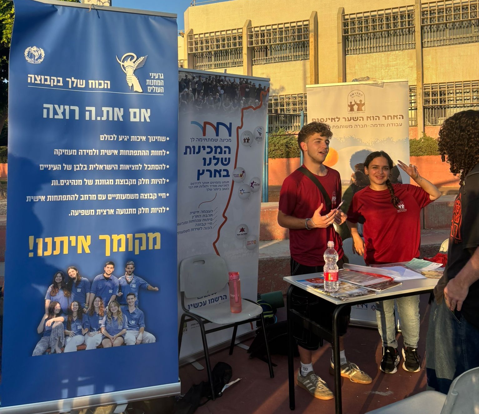 נער ונערה בחולצות אדומות בכנס שנת שירות באשדוד ושלט שכתוב עליו גרעיני המחנות העולים