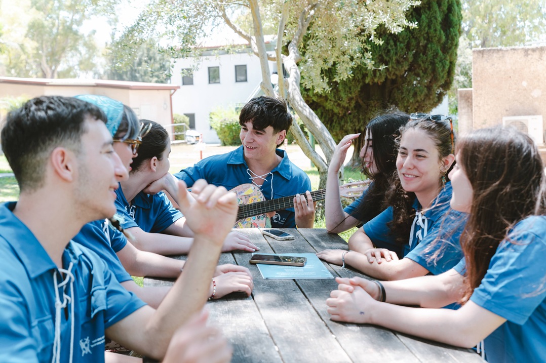 בני ובנות נוער בחולצות כחולות יושבים ליד שולחן עץ