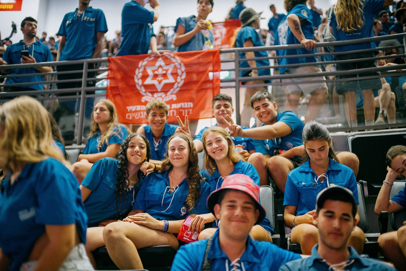 בני נוער בחולצות כחולות יושבים ביציע של אולם ספורט